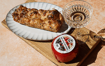 Swavory croissant pull-apart bread with melted Henri Willig Chili Cow Cheese and hot honey, served on a wooden board with a glass of wine.