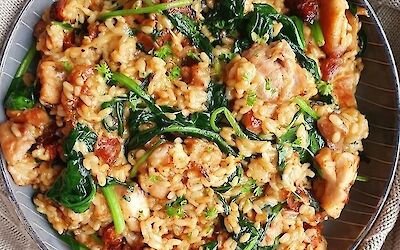 Creamy risotto with spinach, chunks of chorizo and melted cheese served on a dark plate, garnished with fresh parsley.